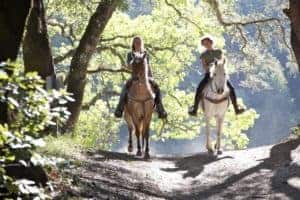 Two girls riding horses through the woods
