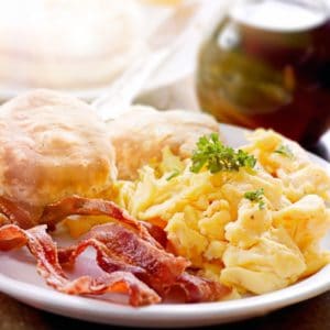 Scrambled eggs, bacon, and biscuits on white plate