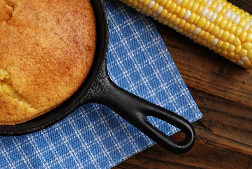 Southern style cornbread in a cast iron skillet next to an ear of corn