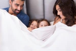 Family snuggled in bed in hotel room