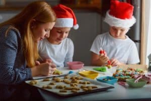 kids decorating cookies with their mom wearing santa hats